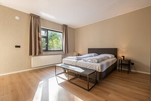 A bedroom with a bed, bedside tables, a bench, a window with curtains, and a radiator.