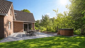A backyard with a patio, a hot tub, and a brick house. - Vakantiepark De Wiltzangh - De Havezate Wellness (Ruinen)