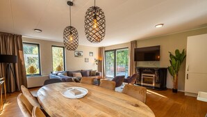 A spacious living area with a wooden dining table, comfortable seating, a fireplace, and large windows. - Vakantiepark De Wiltzangh - De Havezate Wellness (Ruinen)