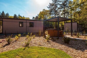 Eine moderne Blockhütte mit überdachter Terrasse, umgeben von bewaldeter Landschaft.