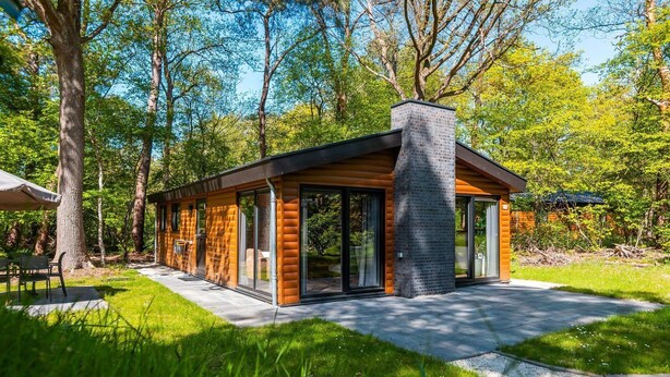 A modern log cabin with a chimney, large glass doors, and a patio area. - De Wiltzangh - Esborg Lodge Hottub | 6p (Ruinen)