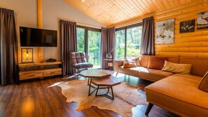 A cozy living room with a wooden ceiling, a leather sofa, a wooden coffee table, and a television on a wooden stand. - De Wiltzangh - Esborg Lodge Hottub | 6p (Ruinen)