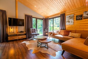 A cozy living room with a wooden ceiling, a leather sofa, a wooden coffee table, and a television on a wooden stand. - De Wiltzangh - Esborg Lodge Hottub | 6p (Ruinen)