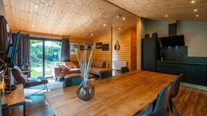 A wooden interior with a dining table, chairs, a sofa, and a kitchen area. - De Wiltzangh - Esborg Lodge Hottub | 6p (Ruinen)