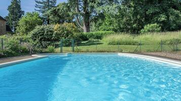 A rectangular swimming pool with a clear blue water surface, surrounded by a low fence and lush greenery including trees and shrubs.