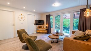 A modern living room with a sofa, chairs, a coffee table, a TV, and a sliding glass door to the outdoors. - De Wiltzangh - Houtenborg Lodge | 4p (Ruinen)
