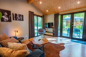 A spacious living room with a wooden ceiling, a large TV, a sofa, a chair, and a rug. - De Wiltzangh - Sterrenborg Lodge | 4p (Ruinen)