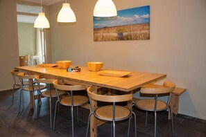 Ein Essbereich mit einem langen Holztisch, sechs Hockern und zwei Pendelleuchten.