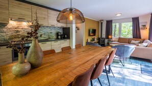 Eine moderne Küche mit Steinrückwand, eine Essecke mit Holztisch und ein Wohnzimmer mit Sofa und Kamin.