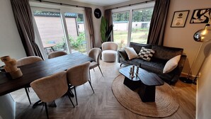 Una sala de estar moderna con una mesa de comedor, sofá y mesa de centro, ventanas amplias y vistas al exterior.