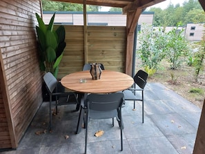Ein Holztisch mit Stühlen, einer Vase und einem Blumentopf auf einer Terrasse.