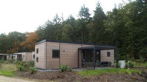Een modern gebouw met een overdekt terras, gelegen in een natuurrijke bosrijke omgeving.