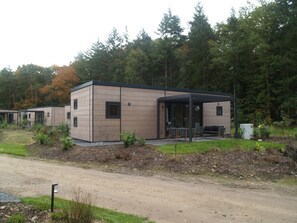 A modern building with a covered outdoor seating area, surrounded by a natural forest setting. - Groeneborg Lodge | 6p (Ruinen)