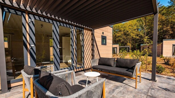 Een terras met rieten stoelen en een bank, een klein rond tafeltje en een glazen deur die naar een kamer leidt.