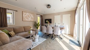 Een moderne woonkamer met een bank, een eettafel met stoelen en een aan de muur bevestigde televisie.