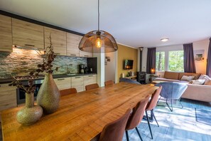A modern kitchen with a stone backsplash, a dining area with a wooden table, and a living room with a sofa and a fireplace. - De Wiltzangh - Vennenborg Lodge Hottub | 6p (Ruinen)