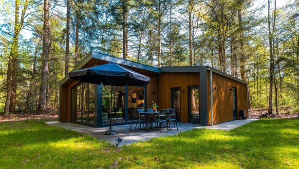 Une cabane moderne dotée d’une paroi vitrée, d’un espace salon extérieur et surplombant une forêt.