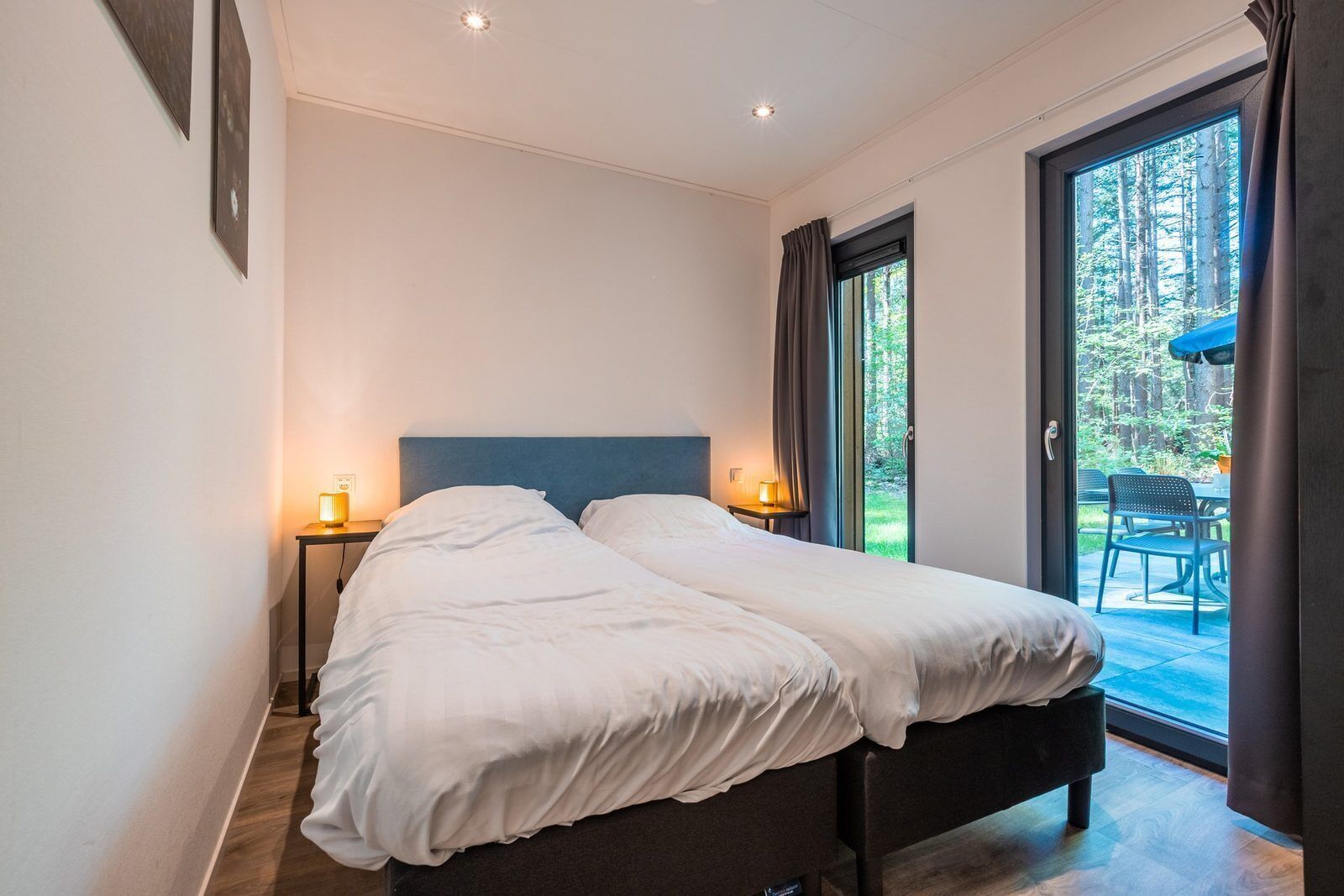 A double bed with a dark headboard, two bedside lamps, and a view of a patio with outdoor furniture.