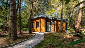 Une cabane en bois, avec un chemin de gravier menant à l’entrée, entourée d’arbres.