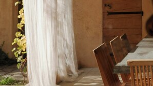 Una stanza con un tavolo e sedie in legno, un'ampia finestra vista su un edificio e una porta con maniglia in metallo.