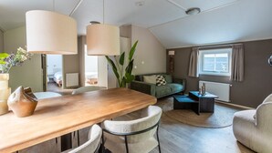 A modern living room with a wooden dining table, two chairs, a sofa, a coffee table, and a large plant. - De Wiltzangh - Veenborg Lodge | 4p (Ruinen)
