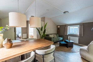 Ein modernes Wohnzimmer mit einem Holzesstisch, zwei Stühlen, einem Sofa, einem Couchtisch und einer großen Pflanze.