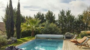Een rechthoekig zwembad met een houten terras, omringd door hoge bomen en een palmboom.