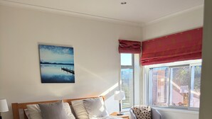 A bedroom with a bed, a nightstand, a lamp, a window with a view, and a painting on the wall.