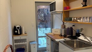 A compact kitchen with a microwave, toaster, and sink. There is a small cabinet with a coffee maker and a basket with bread.