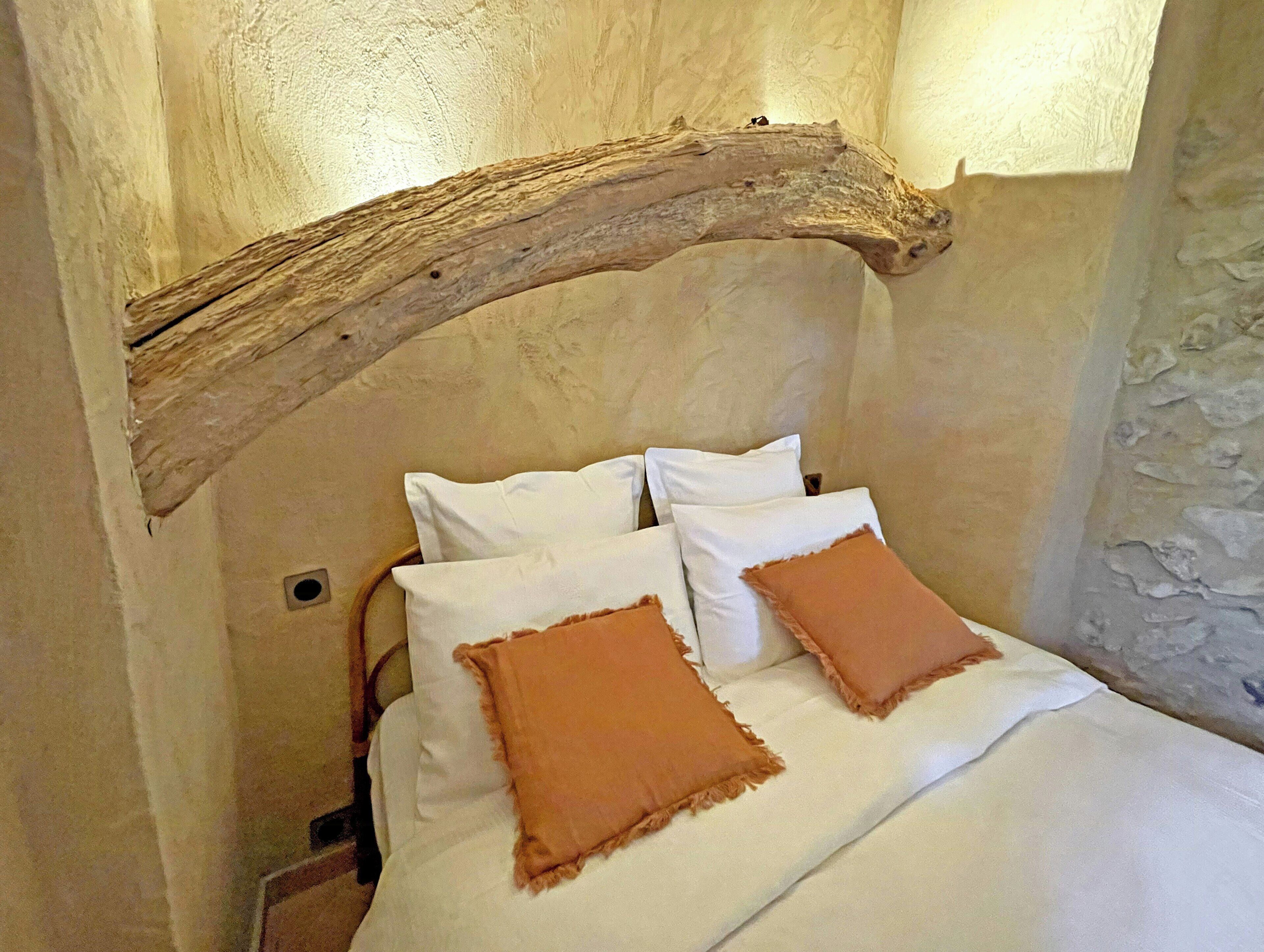 A bedroom with a rustic wooden beam ceiling, white bedding, and two brown pillows.