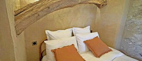A bedroom with a rustic wooden beam ceiling, white bedding, and two brown pillows.