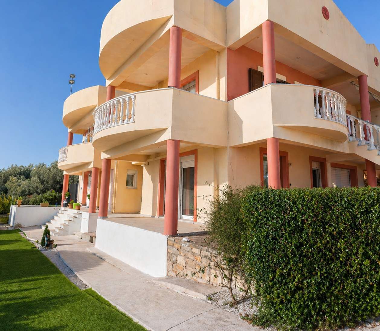 A multi-story building with balconies, a stone base, and a well-maintained lawn.