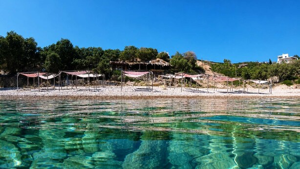 A beach with clear water, umbrellas, and a building in the background. - Nefeli Sea View Stay - Mastiha Grove Suite, Chios (Chios)