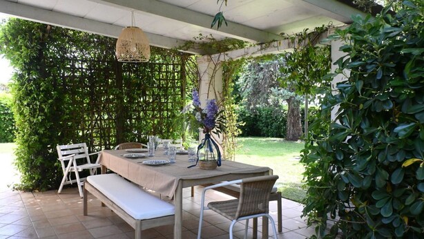 Eine Terrasse im Freien mit einem Essplatz, umgeben von Grünpflanzen und einer Pergola.