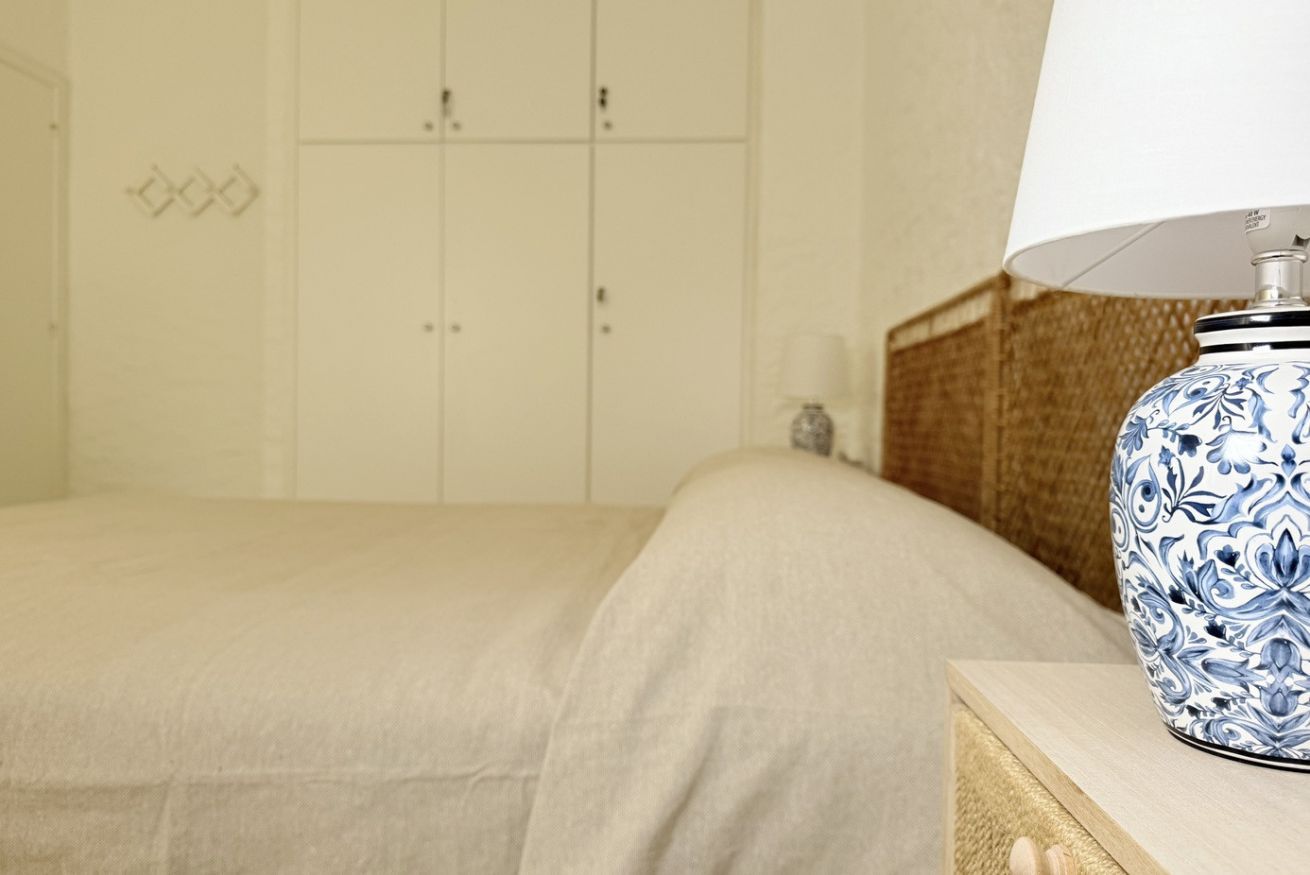 A bedroom with a bed, a nightstand with a lamp, and a wardrobe.