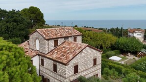 Ein Gebäude aus Stein mit Ziegeldach, umgeben von Grün und Blick auf das Meer.