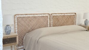Ein Bett mit einem gewebten Kopfteil, ein Nachttisch mit einer Vase und eine Lampe auf einem Beistelltisch.