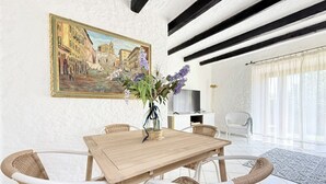 Ein Essbereich mit Holztisch und Korbstühlen, einem Bild an der Wand und einer modernen Küche im Hintergrund.