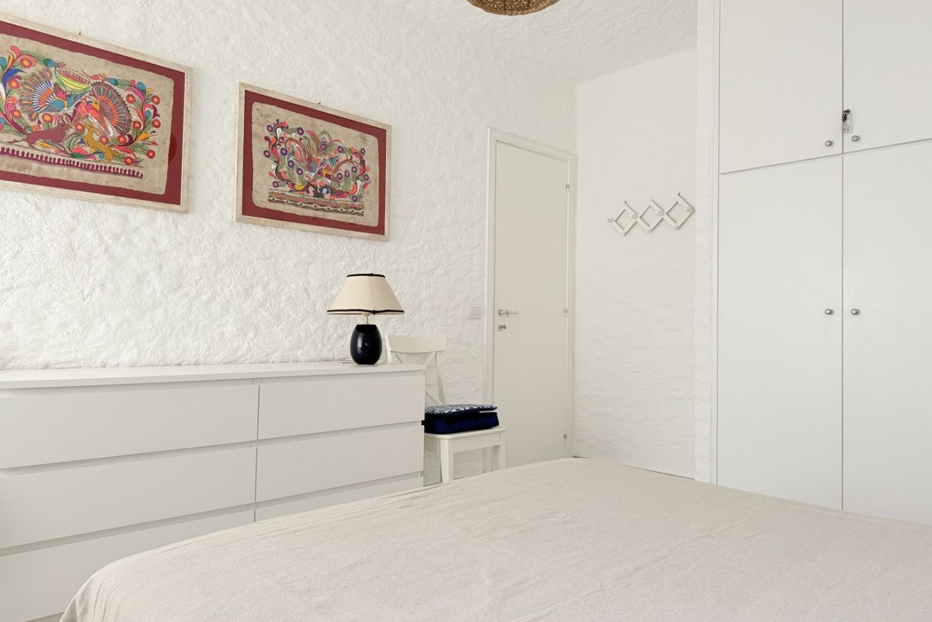 A bedroom with a bed, a dresser, a chair, a lamp, and two framed pictures on the wall.