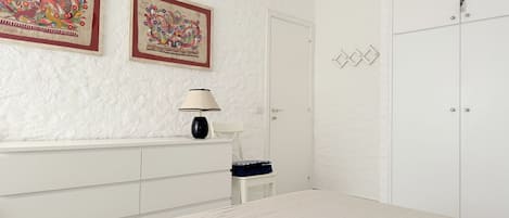 A bedroom with a bed, a dresser, a chair, a lamp, and two framed pictures on the wall.