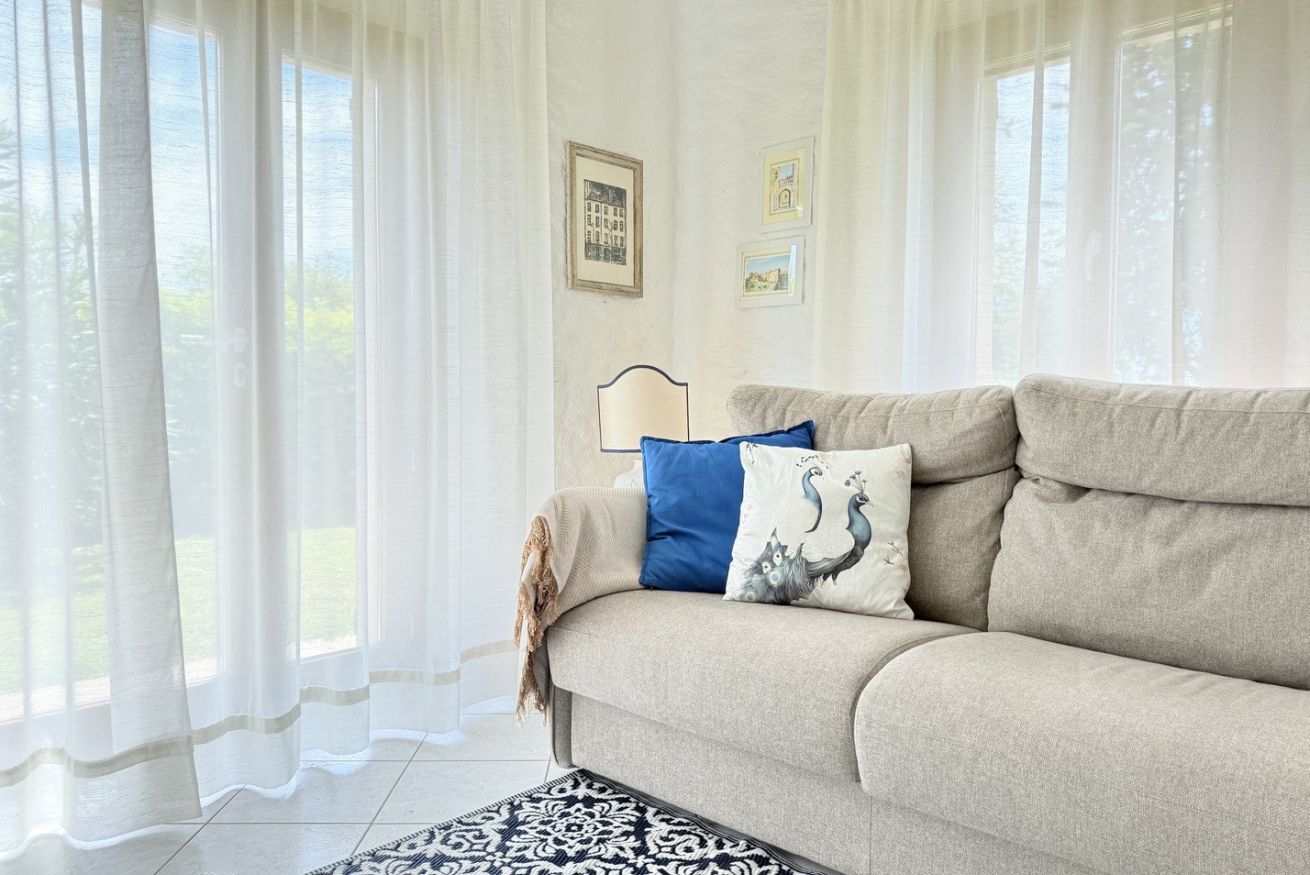 Un salon avec un canapé, un tapis à motifs et des rideaux légers.