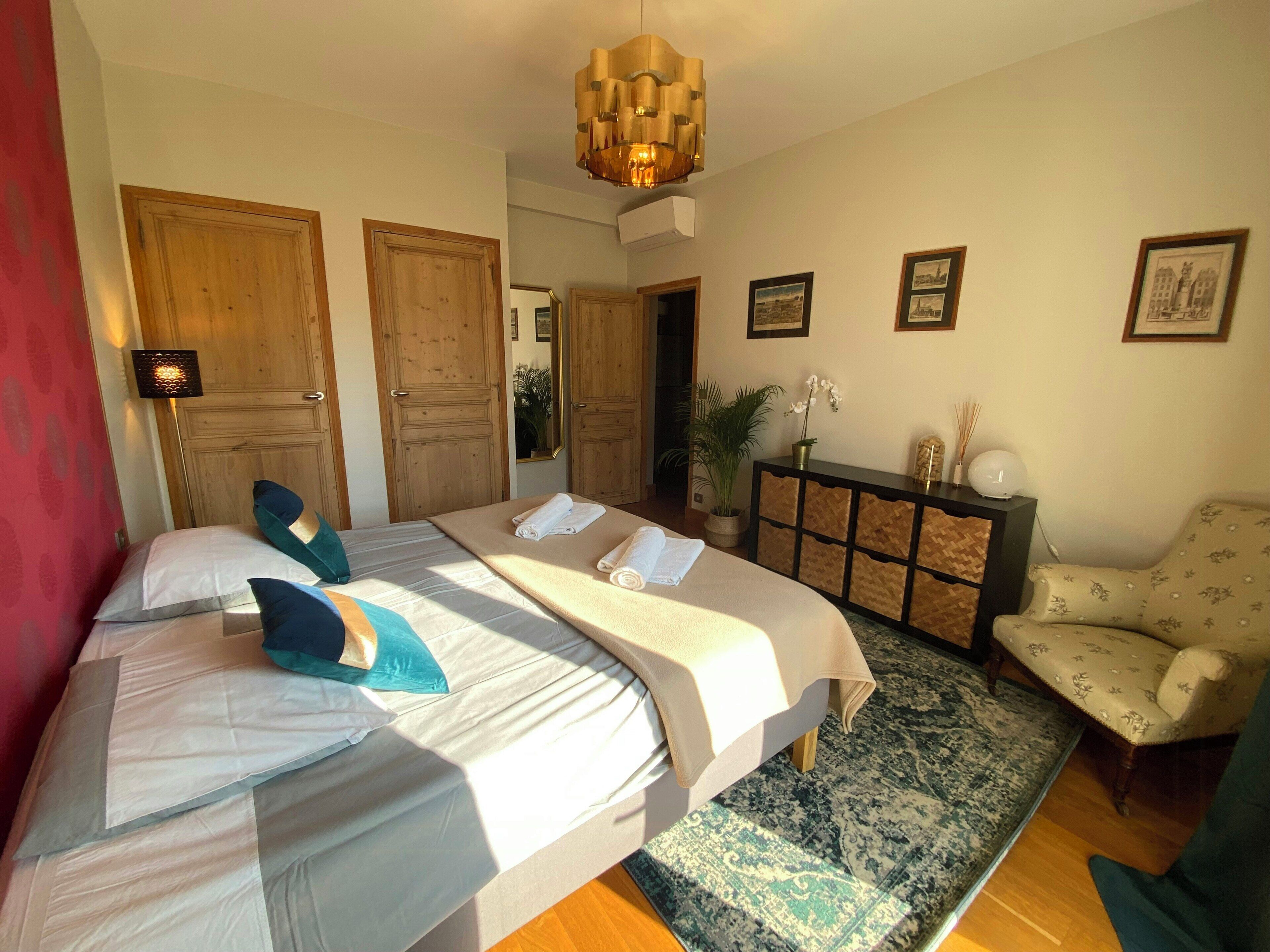 A hotel room with a large bed, a desk, a chair, a mirror, and a potted plant.