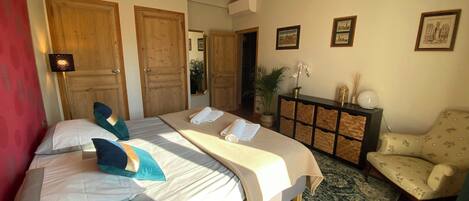 A hotel room with a large bed, a desk, a chair, a mirror, and a potted plant.