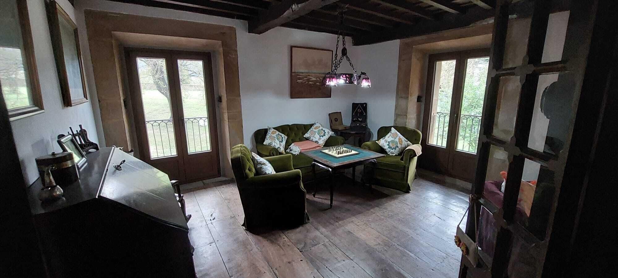 A room with a wooden floor, a green sofa set, a chess table, and a hanging light fixture.