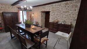 Une pièce aux murs de pierre, avec une table à manger en bois, des bancs et une chaise blanche.