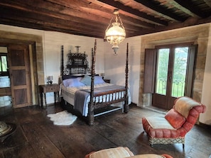 A four-poster bed with a chandelier, a red armchair, and a view of the outdoors through a window. - La Casona de Cabanzón is a rural mountain house surrounded by nature. (Cabanzón)
