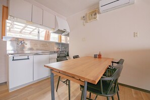 Une cuisine de taille réduite, avec des meubles blancs, une table à manger en bois et une fenêtre donnant sur le jardin.