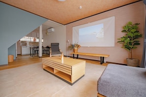 Un salon moderne avec une table basse en bois, un canapé gris, un écran de projection et une plante en pot.