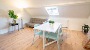 Una habitación pequeña y luminosa con una mesa y sillas blancas, un sofá, una planta en maceta y un tragaluz.