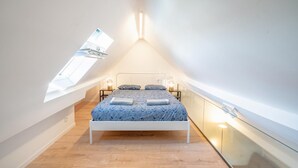 Un dormitorio con techo inclinado, una cama, lámparas de noche y un tragaluz.